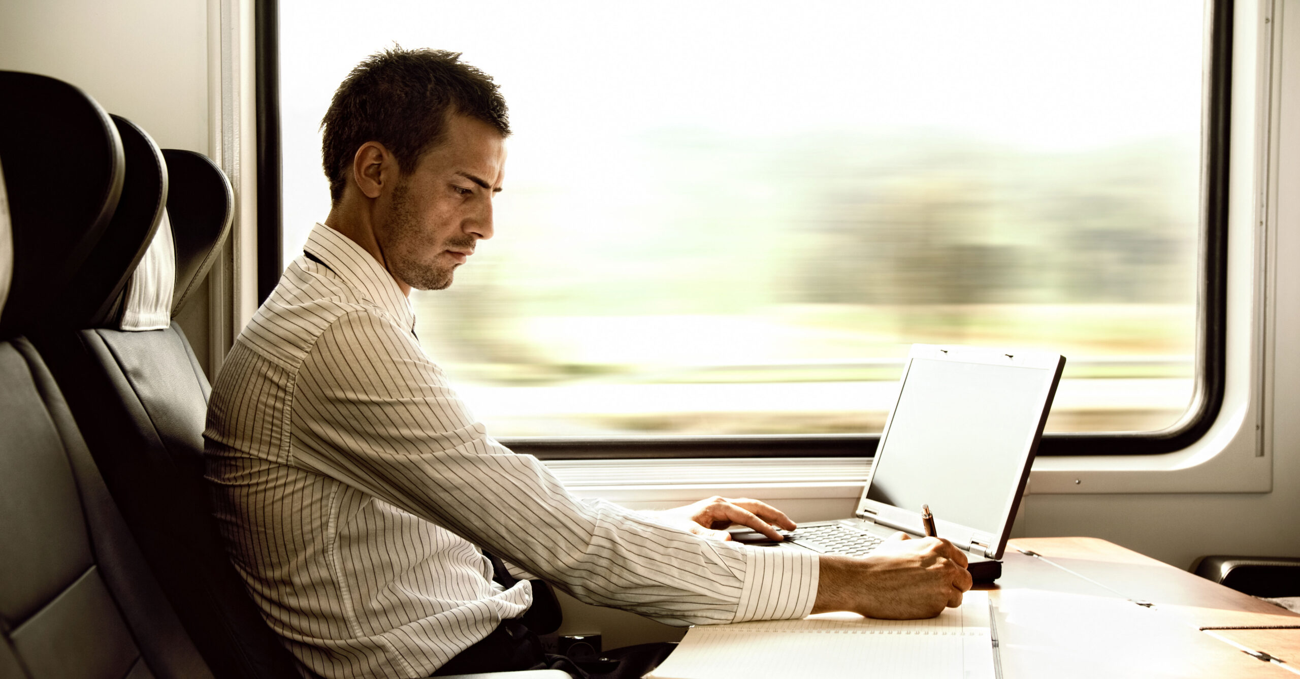 en man som arbetar med laptop på ett tåg - ett exempel på hur verksamheters transporter kan göras hållbara