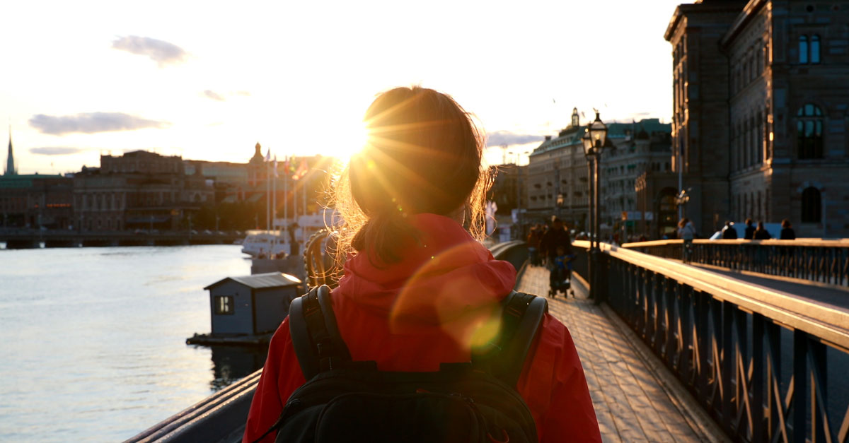 En kvinna går på promenadstråk genom staden medan solen står lågt på himlen.