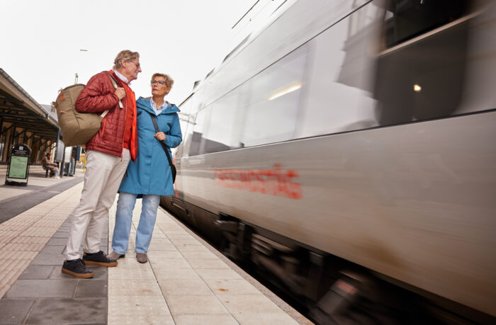 ett par väntar på perrongen när ett tåg passerar